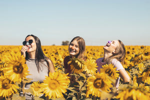 Three friends wearing colorful Nöz sunscreen in a field of sunflowers 